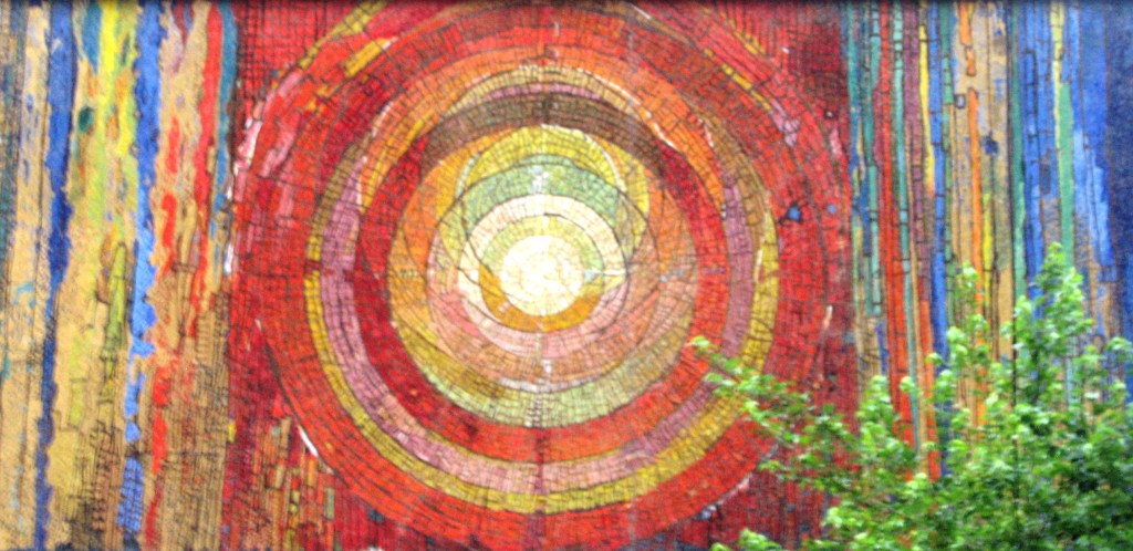 Mosaic on an outer wall creating a circle of yellows, pinks and reds.