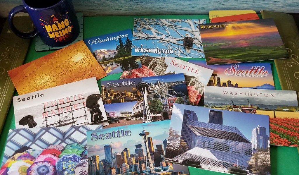 A collection of Seattle-themed postcards on a desk with a blue NaNoWriMo coffee cup.