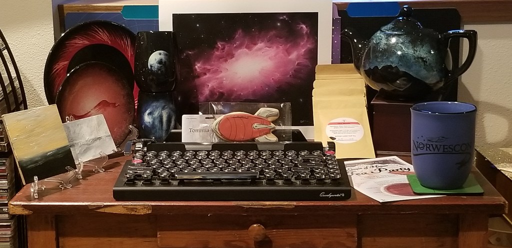 Assorted teacups, miniature paintings, tea bags, a teapot, and a keyboard all cluttered on a desk.