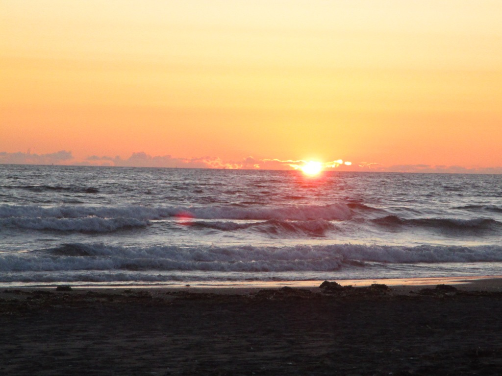 Sun setting over the ocean as waves roll towards the beach