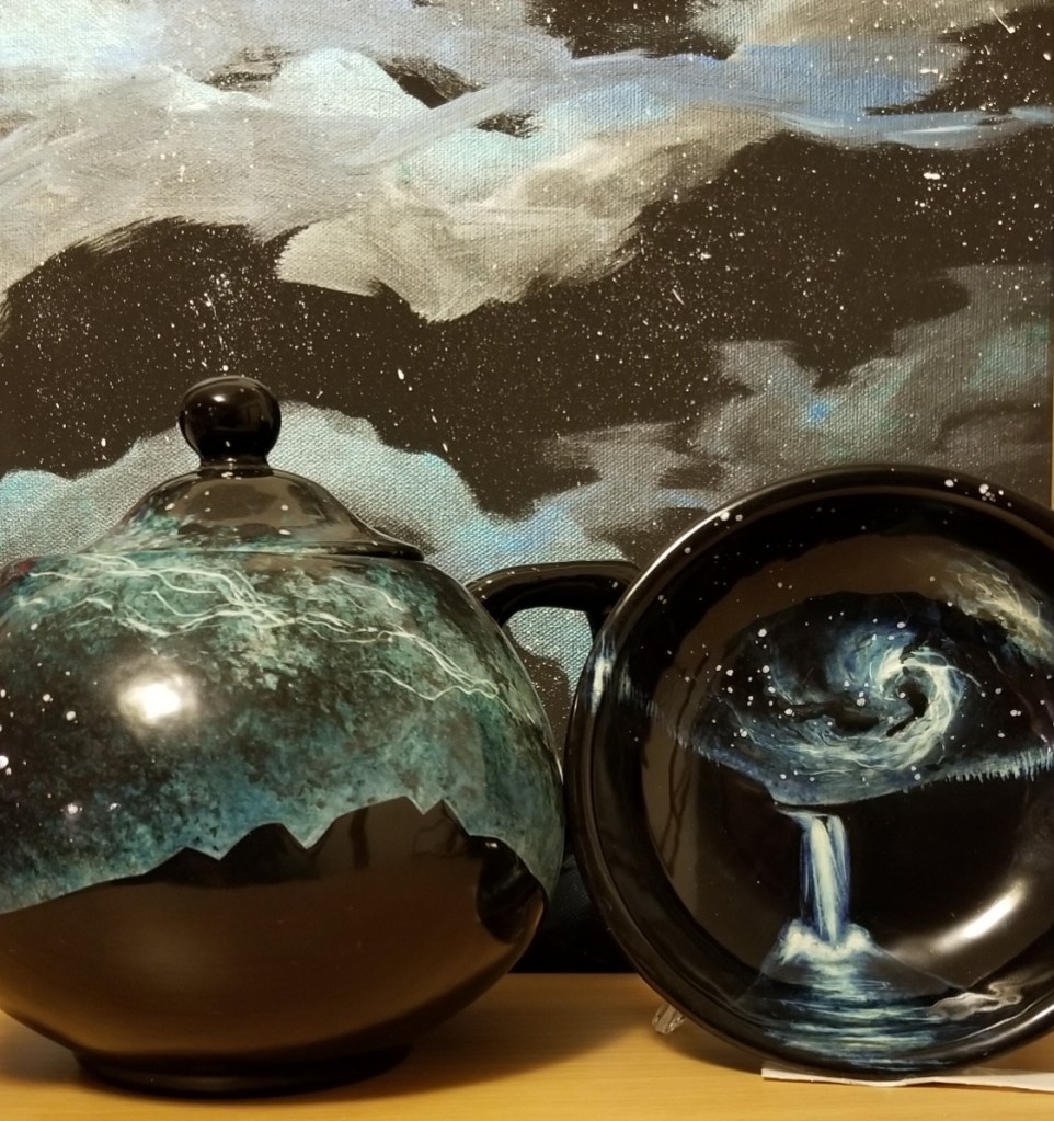 Galactic scene of stars and clouds painted on canvas by Angel Abraham Loo.

In front of it - a ceramic teapot with a black silhouette of Mount Si under the stars and nebula and a small round plate (propped) with Snoqualmie Falls under a cosmic swirl in the star-filled sky - both painted by Amy Rae Hill.