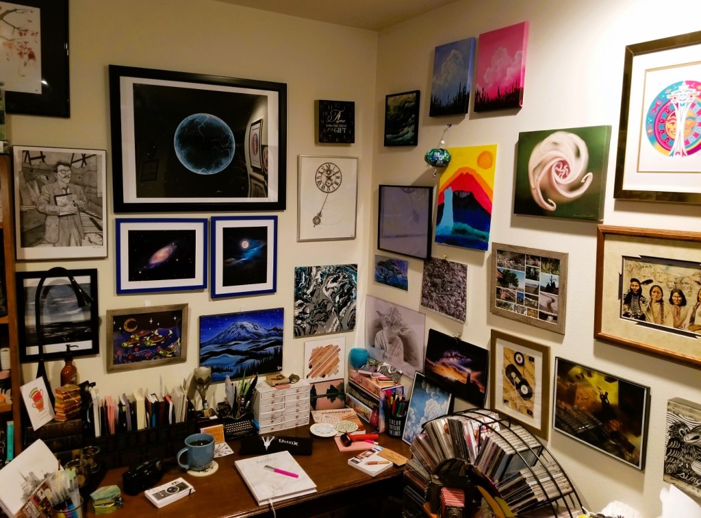 Corner with various photos, paintings and sketches by talented artists.
A table covered with hobby items such as notebooks, sketchbooks, a camera, pens, etc.