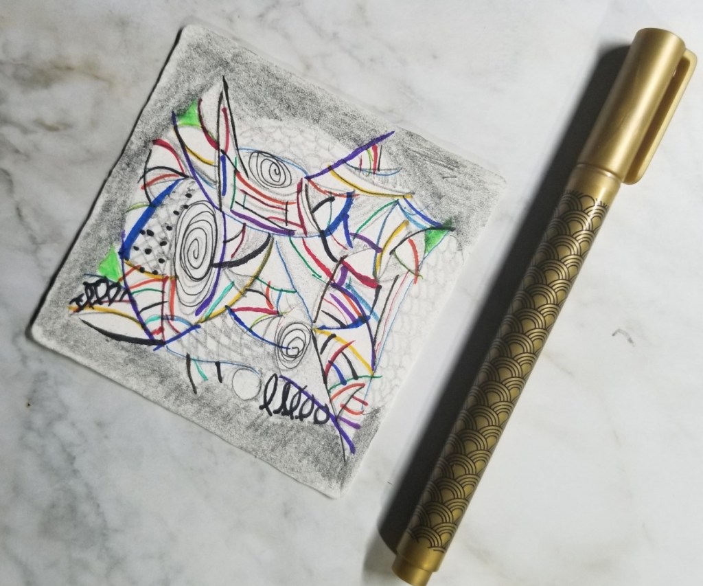 A colorful doodling on a square piece of paper beside a golden pen.