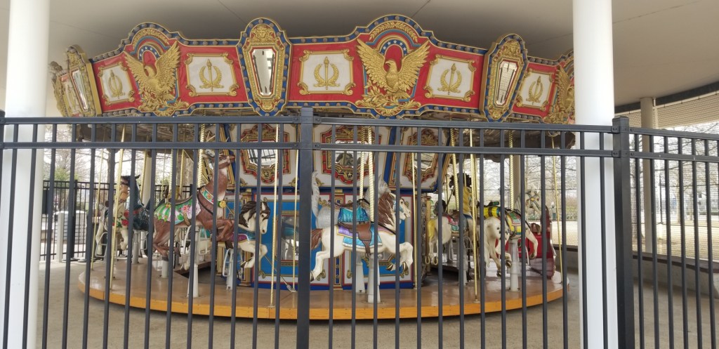 A carousel as seen through a fence in the park.